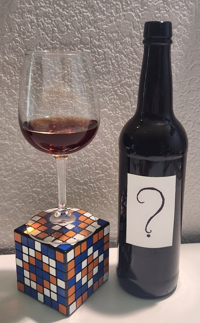 Photo of a wine glass on top of a 7x7x7 Rubik's cube and a wine bottle with a question mark on the label.